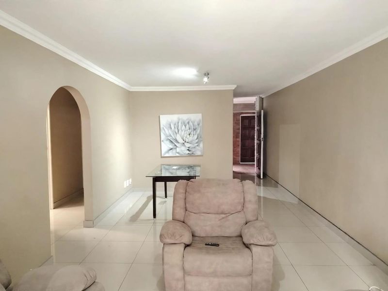 A spacious living area featuring neutral wall tones, tiled flooring, and a distinctive architectural archway leading to adjacent rooms.