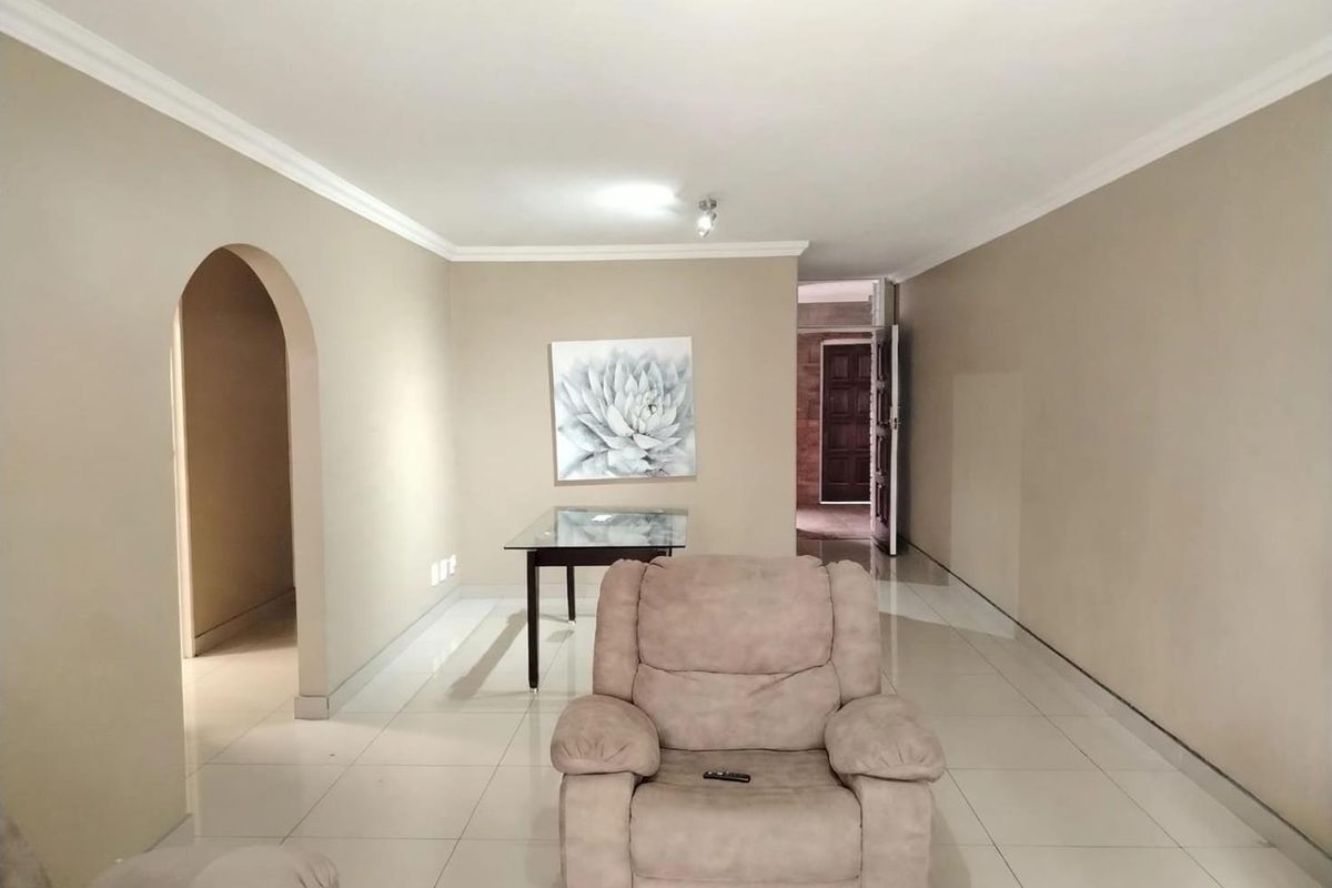 A spacious living area featuring neutral wall tones, tiled flooring, and a distinctive architectural archway leading to adjacent rooms.