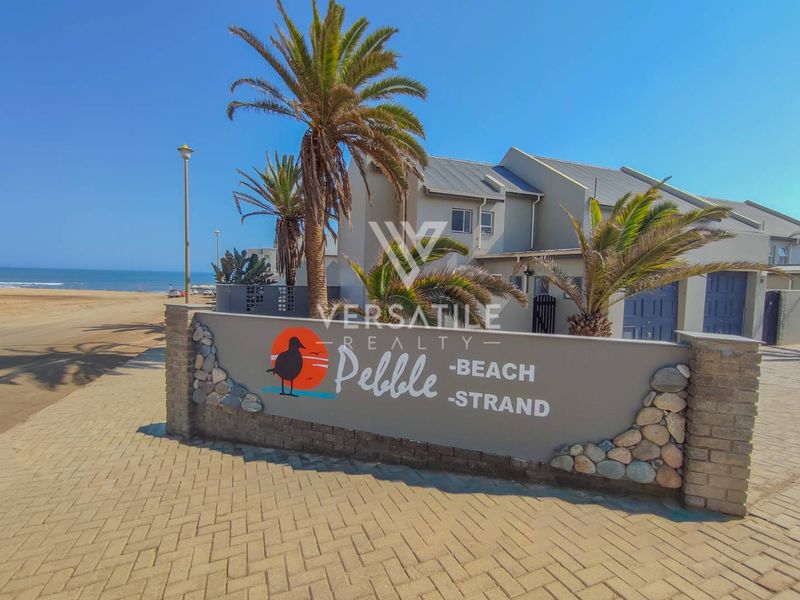 Front entrance view of the Pebble Beach townhouse complex, featuring a paved driveway, boundary wall, and proximity to the coastline.