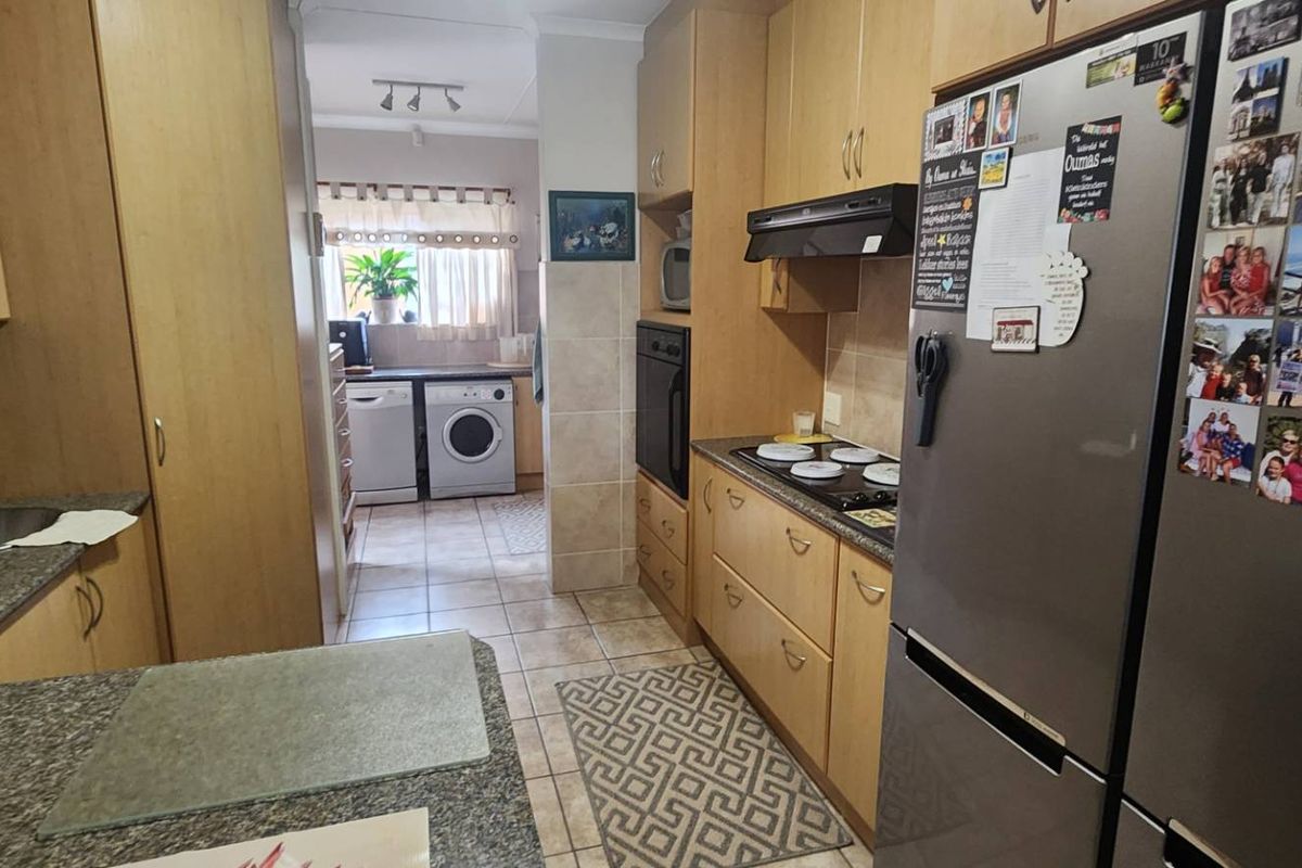Functional kitchen featuring light wood cabinetry, granite countertops, built-in oven, and hob, with an adjoining laundry area.