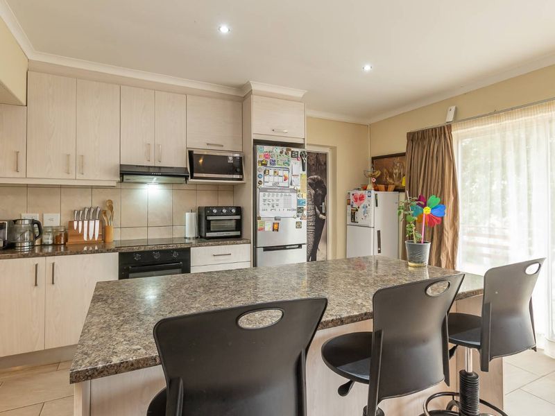 A functional kitchen featuring light-toned cabinetry, a central island with breakfast bar seating, built-in appliances, and a tiled backsplash.