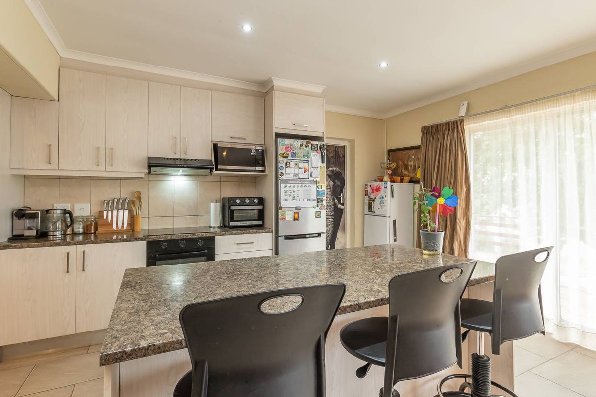 A functional kitchen featuring light-toned cabinetry, a central island with breakfast bar seating, built-in appliances, and a tiled backsplash.