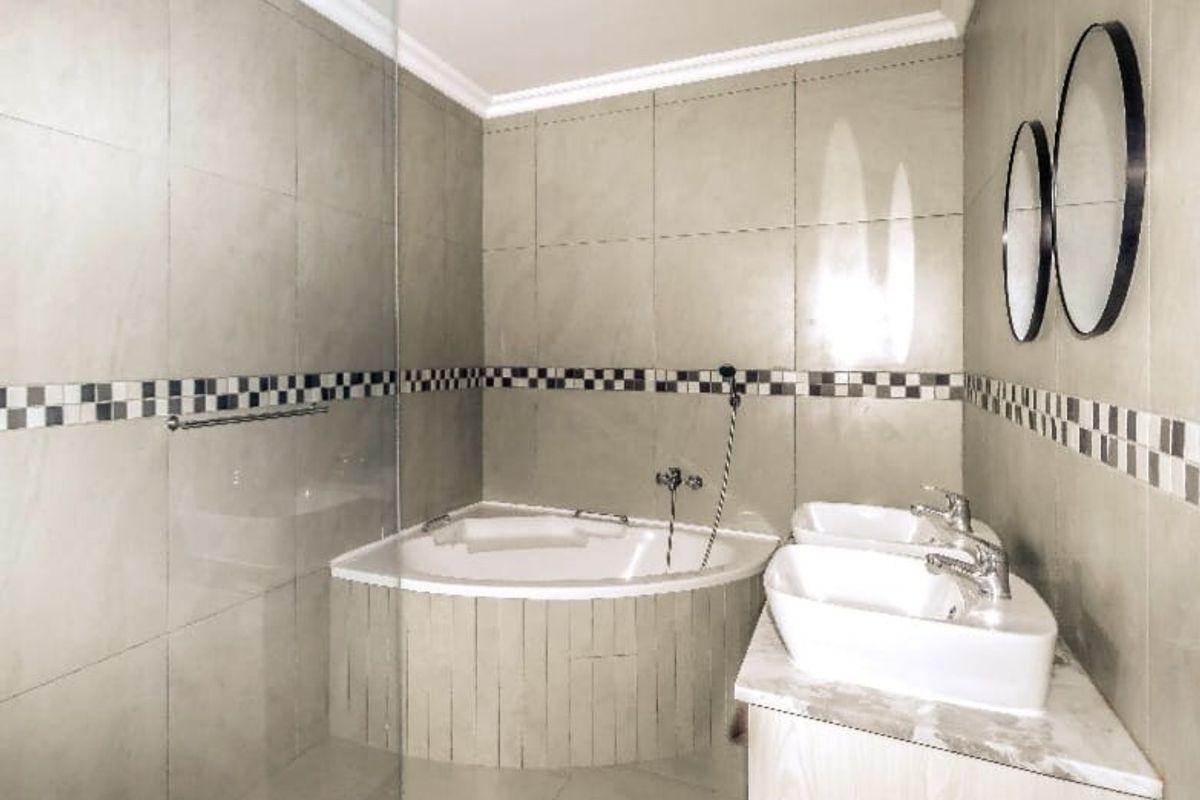 Modern bathroom featuring a corner bathtub, glass shower screen, and a double vanity with contemporary ceramic tiling and a decorative mosaic border.