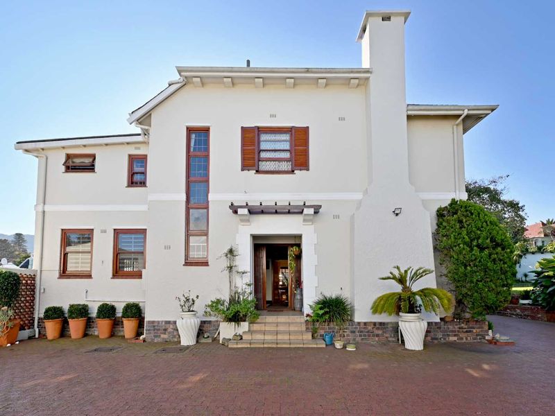 A well-maintained double-story residence featuring a classic plastered facade, prominent chimney, timber-framed windows with shutters, and a paved driveway entrance.