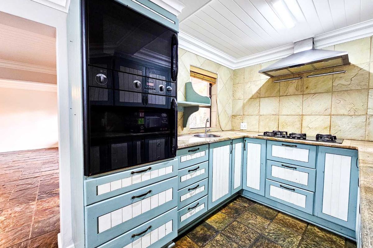 A functional kitchen featuring built-in oven, gas hob, extractor fan, stone countertops, and tiled flooring with ample storage cabinetry.