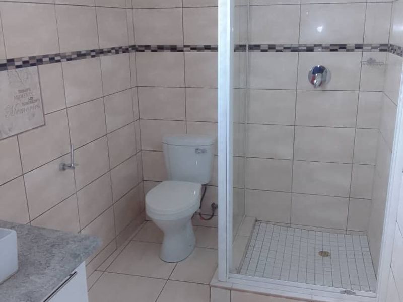 A clean, functional bathroom featuring a glass-enclosed shower, a white toilet, and a vanity cabinet with a stone countertop.
