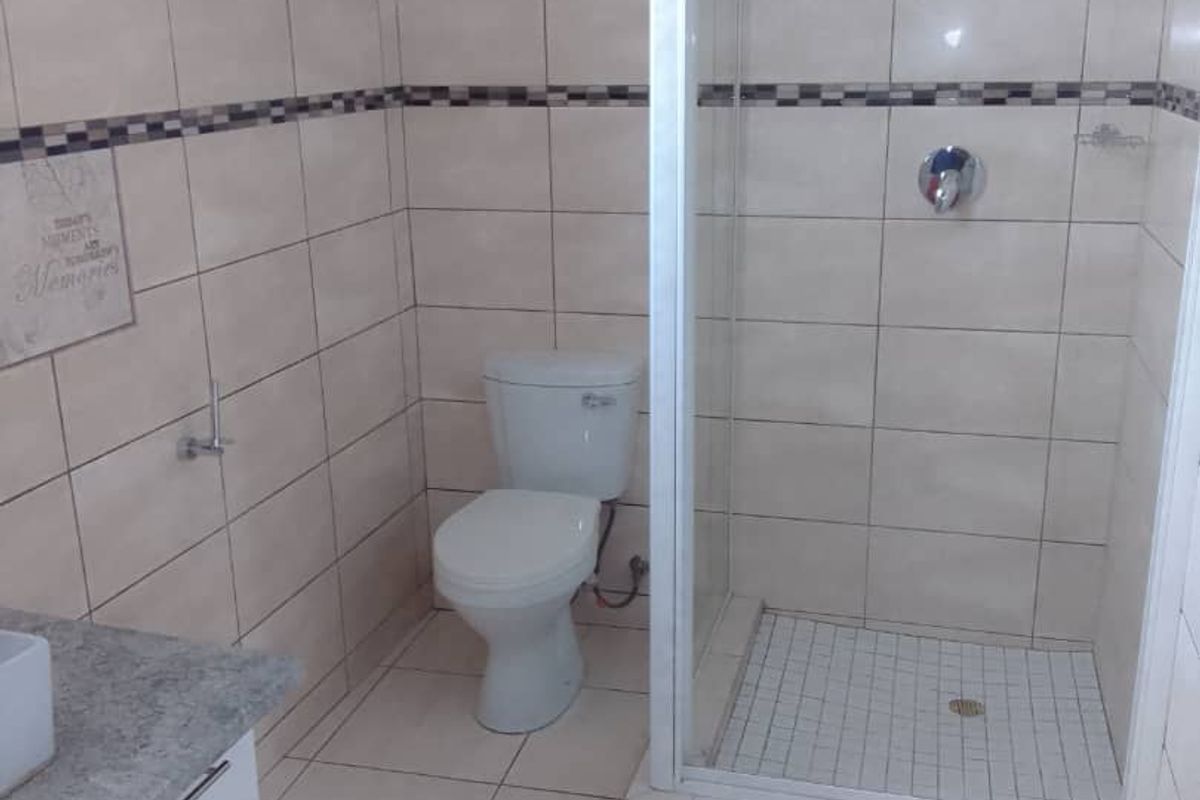 A clean, functional bathroom featuring a glass-enclosed shower, a white toilet, and a vanity cabinet with a stone countertop.