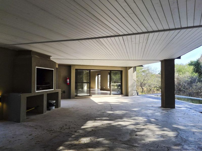 Spacious covered patio featuring a built-in braai, concrete flooring, and large sliding glass doors providing seamless access to the interior living space.