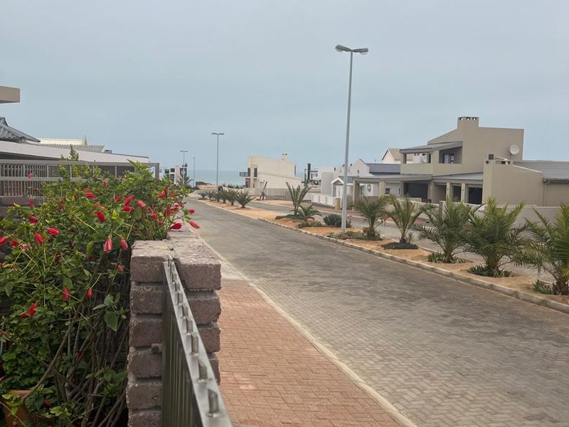 A view of a paved residential street with brick sidewalks, street lighting, and landscaped verges in a coastal neighborhood.