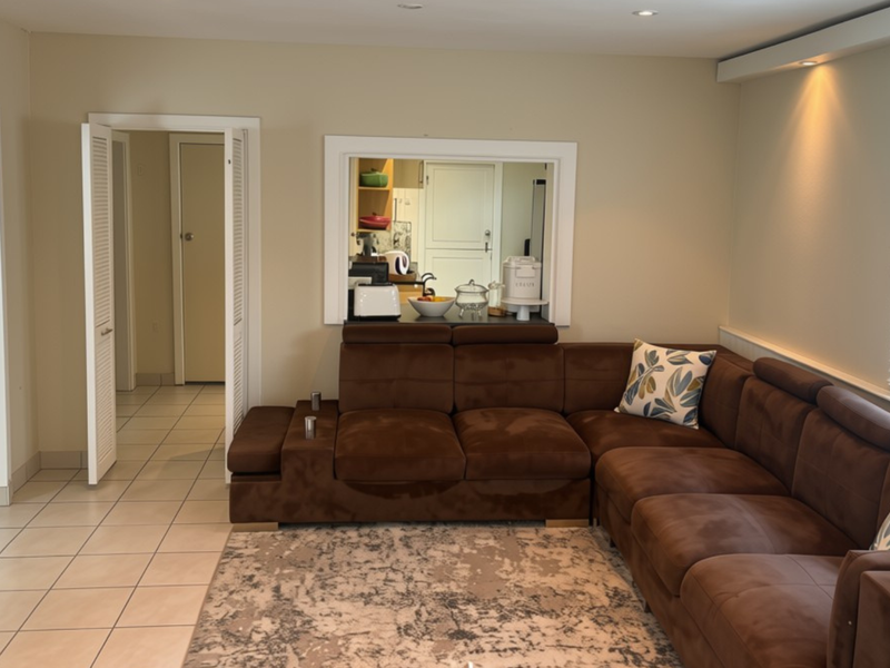 A living room featuring tiled flooring, recessed lighting, and a convenient pass-through window connecting to the kitchen area.