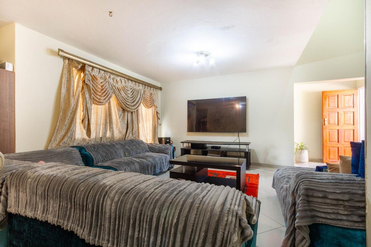 A spacious living room featuring tiled flooring, a wall-mounted television, and a doorway leading to an adjacent area.