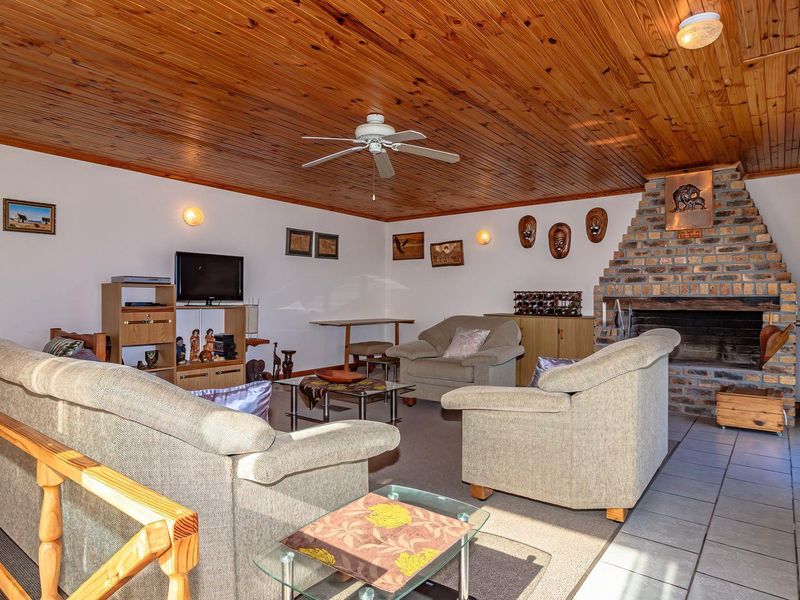 Spacious living room featuring a rustic timber ceiling, a prominent brick fireplace, and tiled flooring, offering a warm and traditional atmosphere.