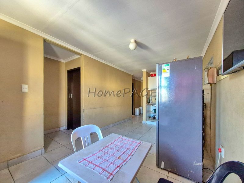 An open-plan living and kitchen area featuring tiled flooring and neutral wall finishes, requiring cosmetic updates to improve the overall aesthetic.