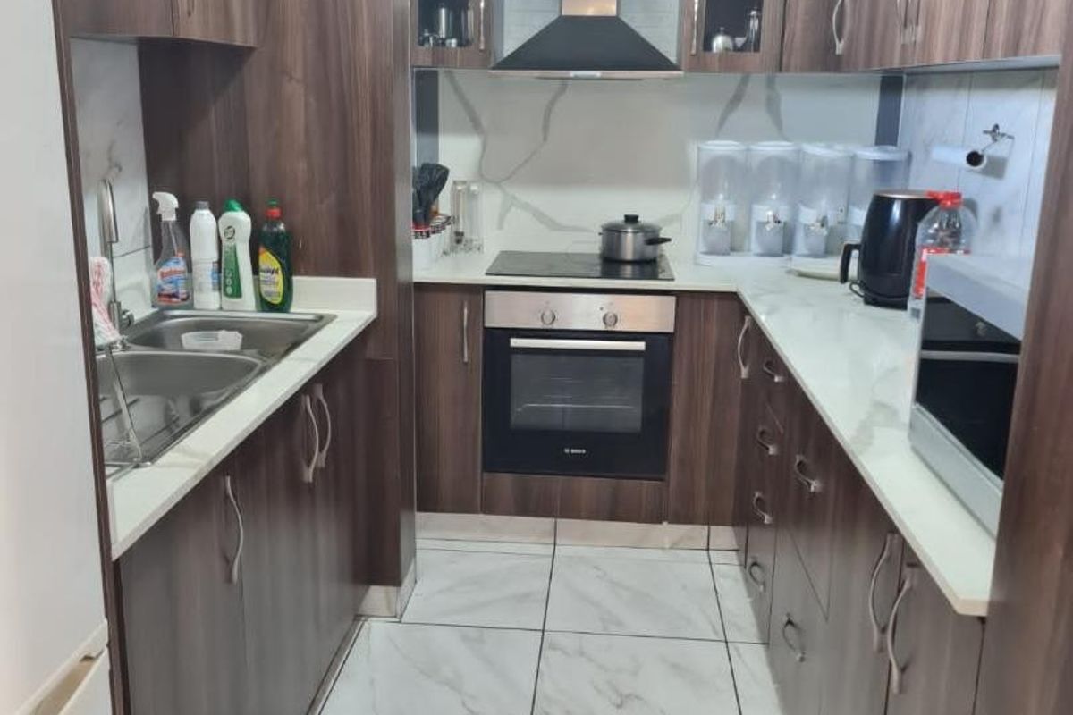 A functional galley-style kitchen featuring dark wood cabinetry, stone countertops, integrated appliances, and modern marble-look floor tiles.