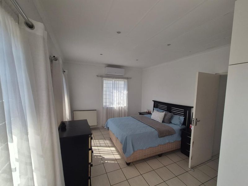 A well-lit bedroom featuring tiled flooring, recessed ceiling lighting, and a wall-mounted air conditioning unit.