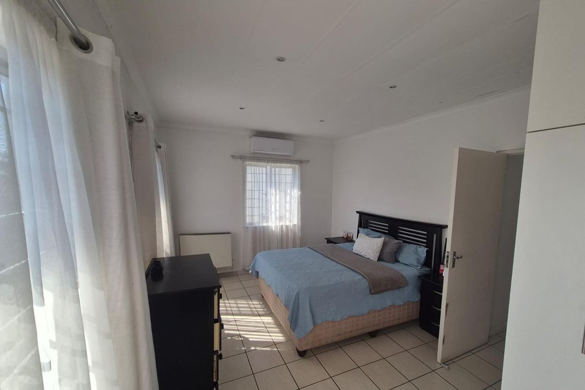 A well-lit bedroom featuring tiled flooring, recessed ceiling lighting, and a wall-mounted air conditioning unit.