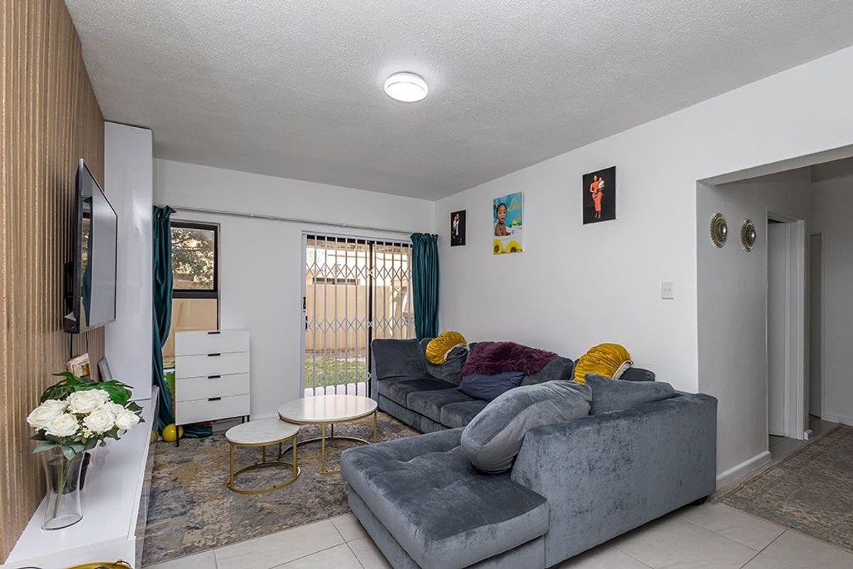 A living room featuring tiled flooring, a sliding glass door with a security gate, and access to an outdoor area.
