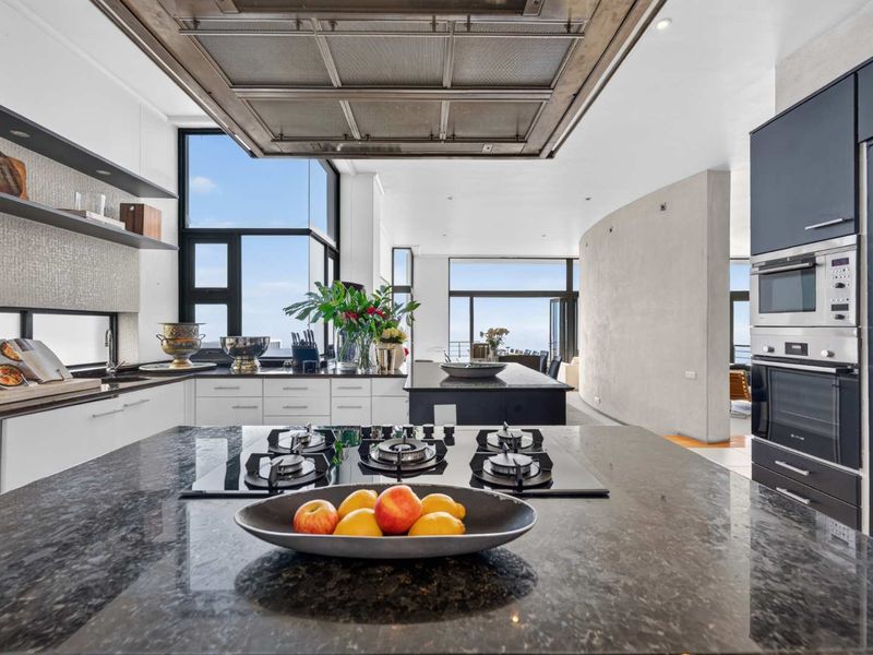 Modern, high-end kitchen featuring a large granite island, gas cooktop, integrated appliances, and expansive windows with natural light.