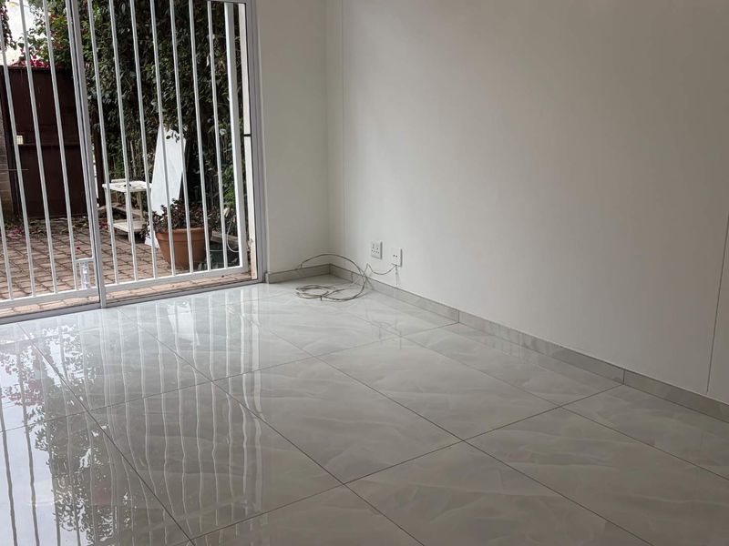 A bright, empty living area featuring polished tiled flooring and a sliding glass door with a security gate leading to an outdoor space.