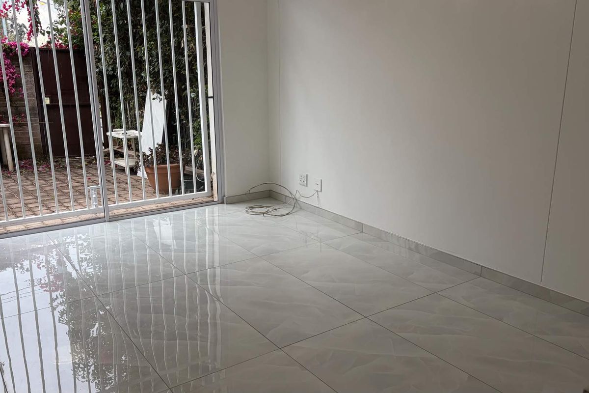 A bright, empty living area featuring polished tiled flooring and a sliding glass door with a security gate leading to an outdoor space.