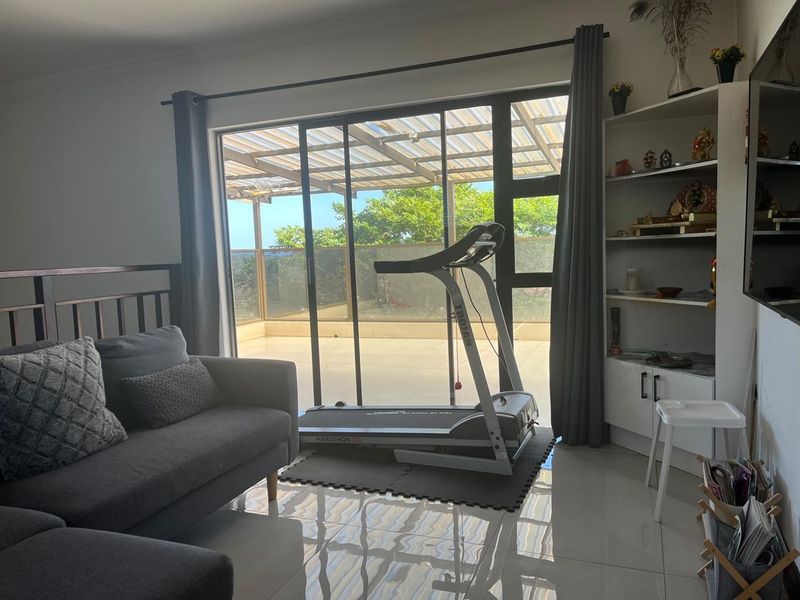 A bright living room featuring large sliding glass doors that open onto a patio, complemented by tiled flooring and a built-in shelving unit.