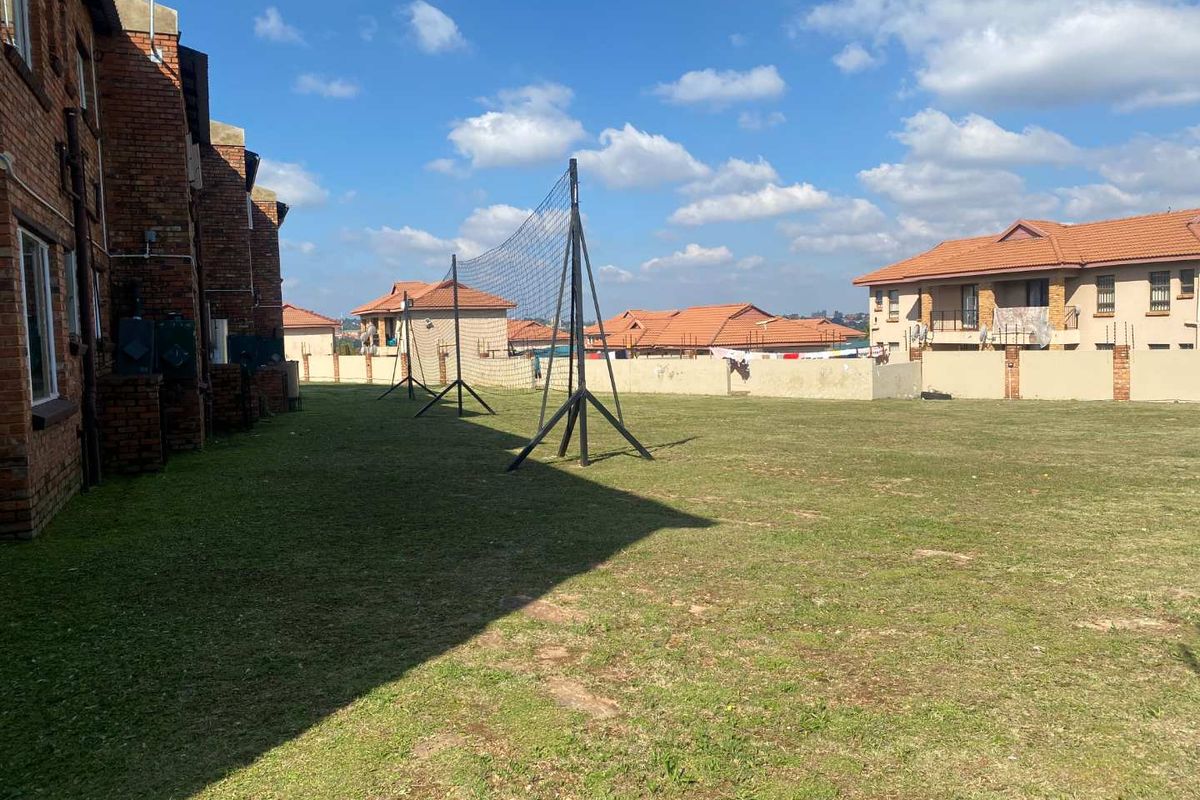 A communal outdoor area featuring a grass lawn and a sports net, situated between apartment buildings in a residential complex.
