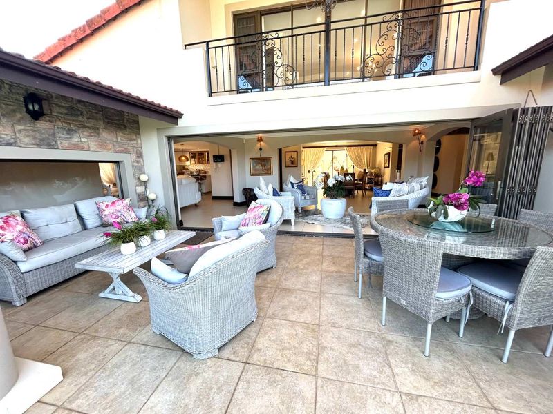 Spacious covered patio featuring tiled flooring, stone accent wall, and seamless indoor-outdoor flow through folding glass doors, leading to an upper-level balcony.