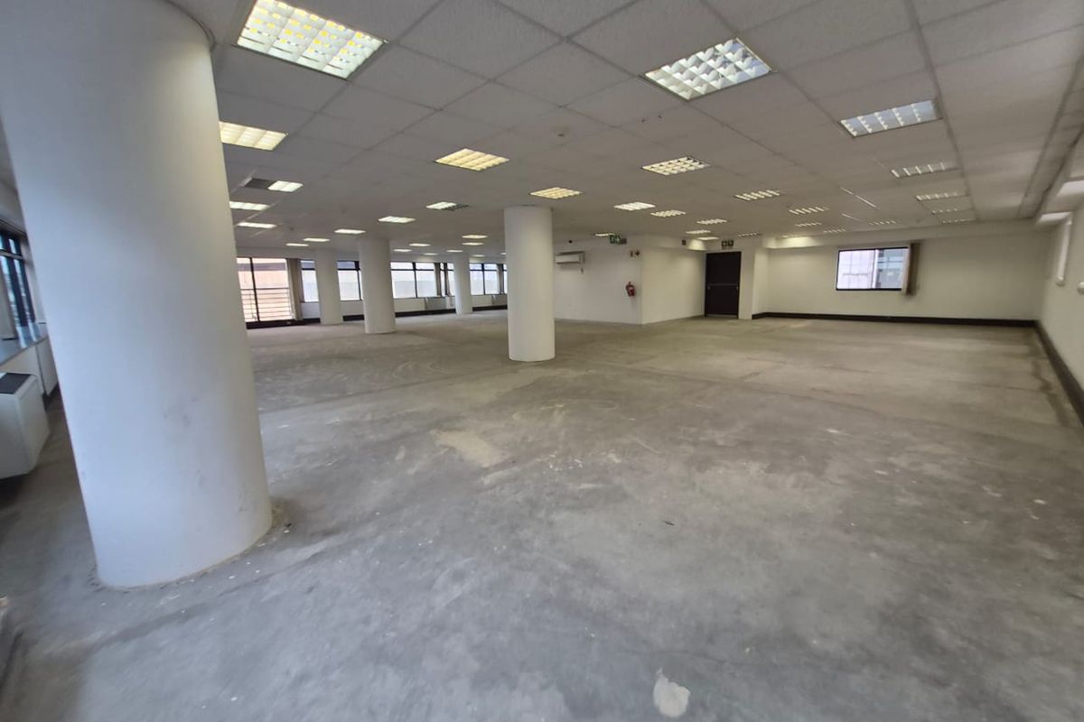 A large, open-plan office space featuring structural columns, a suspended ceiling with recessed lighting, and unfinished concrete flooring, ready for tenant fit-out.
