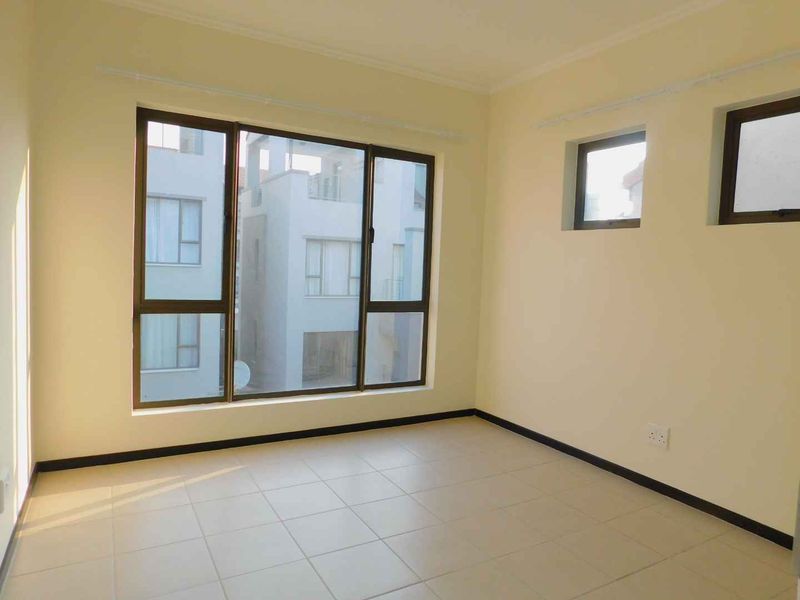 A bright, empty bedroom featuring neutral tiled flooring, large aluminium-framed windows, and clean wall finishes, ready for personalization.