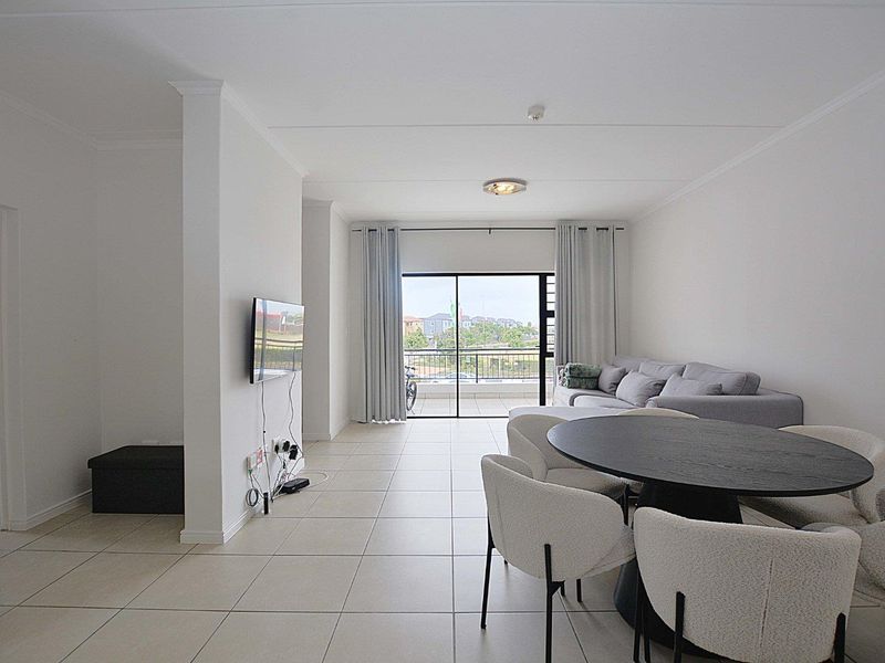 Bright open-plan living and dining area featuring neutral tiled flooring and a large sliding glass door leading to an outdoor balcony.