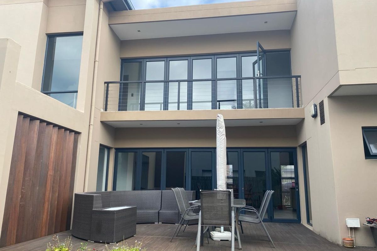 Rear view of the property featuring a timber deck patio, large glass folding doors, and an upper-level balcony with metal railings.