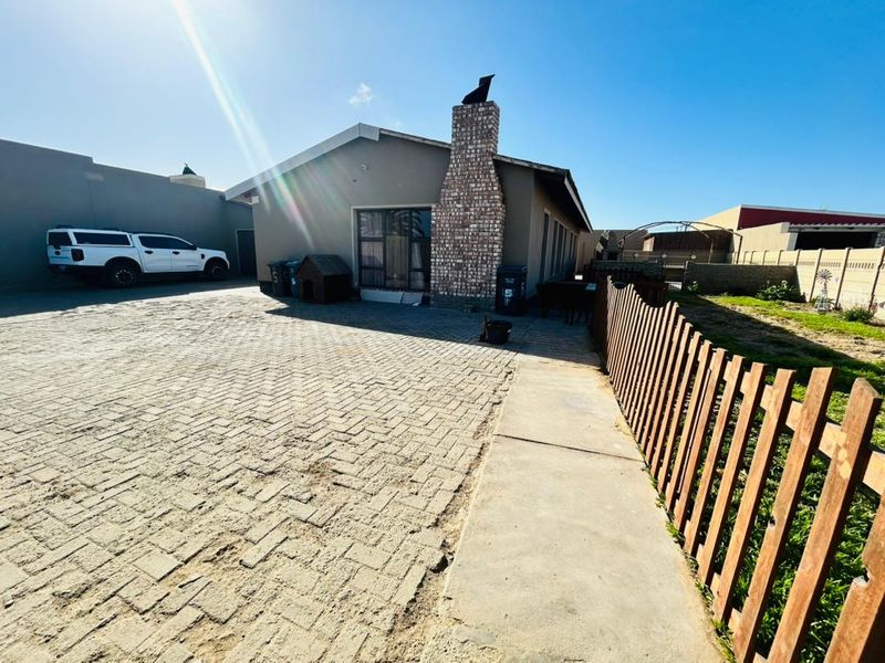Rear exterior view of the house featuring a brick chimney, paved driveway, and wooden fencing.