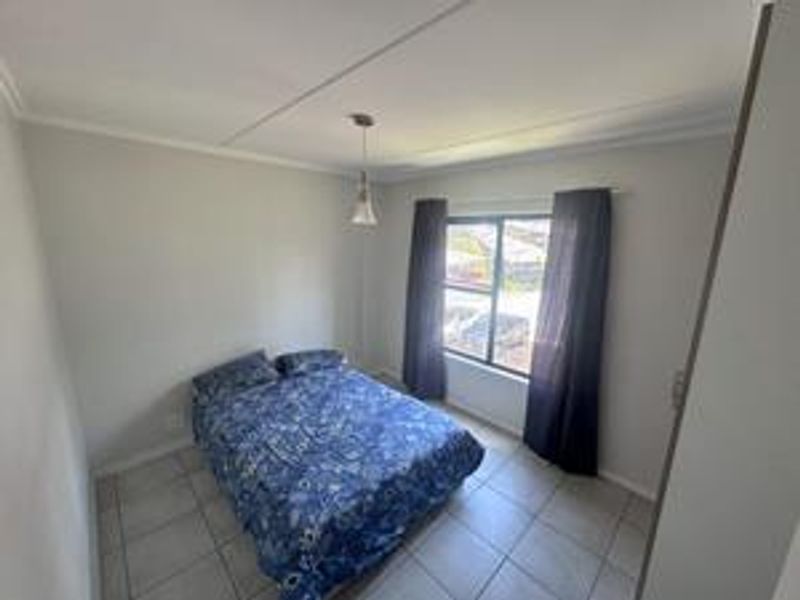 A functional bedroom featuring tiled flooring, a built-in cupboard, and a window providing natural light.