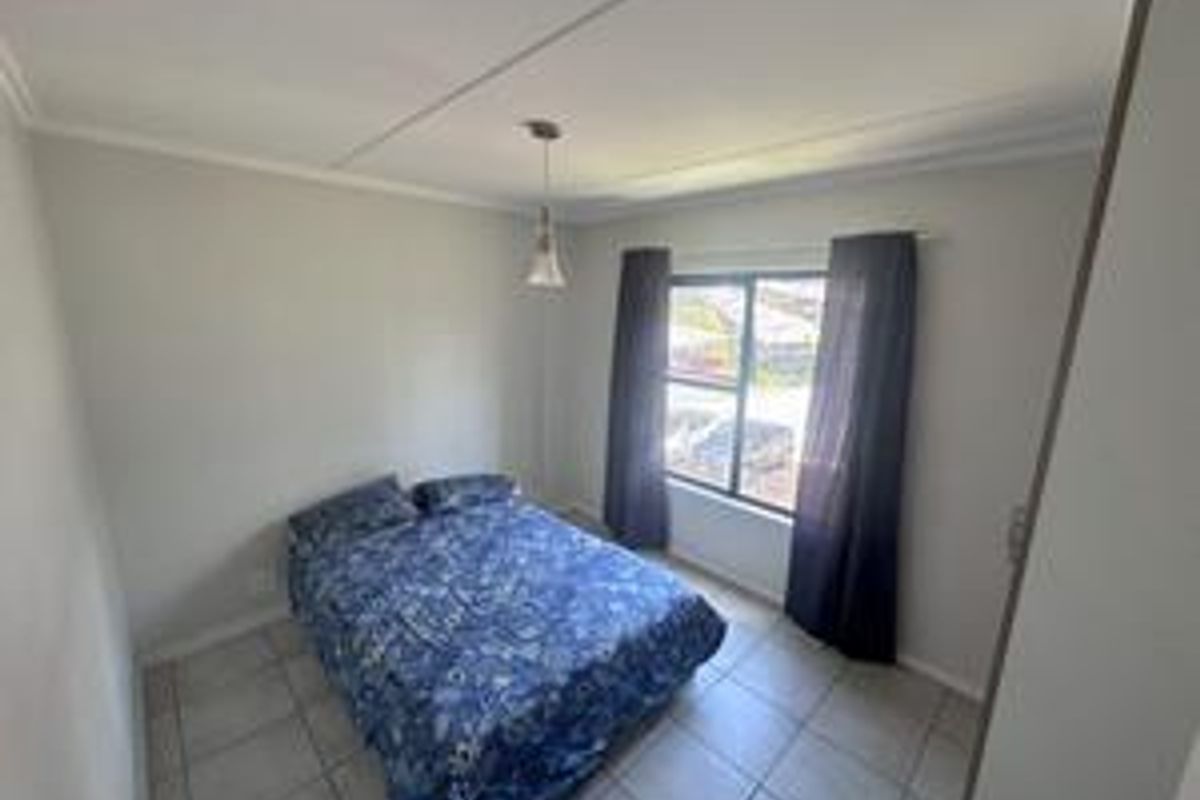 A functional bedroom featuring tiled flooring, a built-in cupboard, and a window providing natural light.