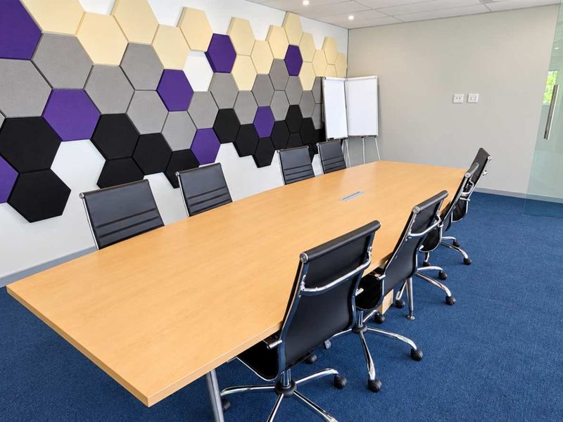 Modern office boardroom featuring acoustic hexagonal wall panels, blue carpeting, and a glass partition wall, providing a professional and functional meeting space.