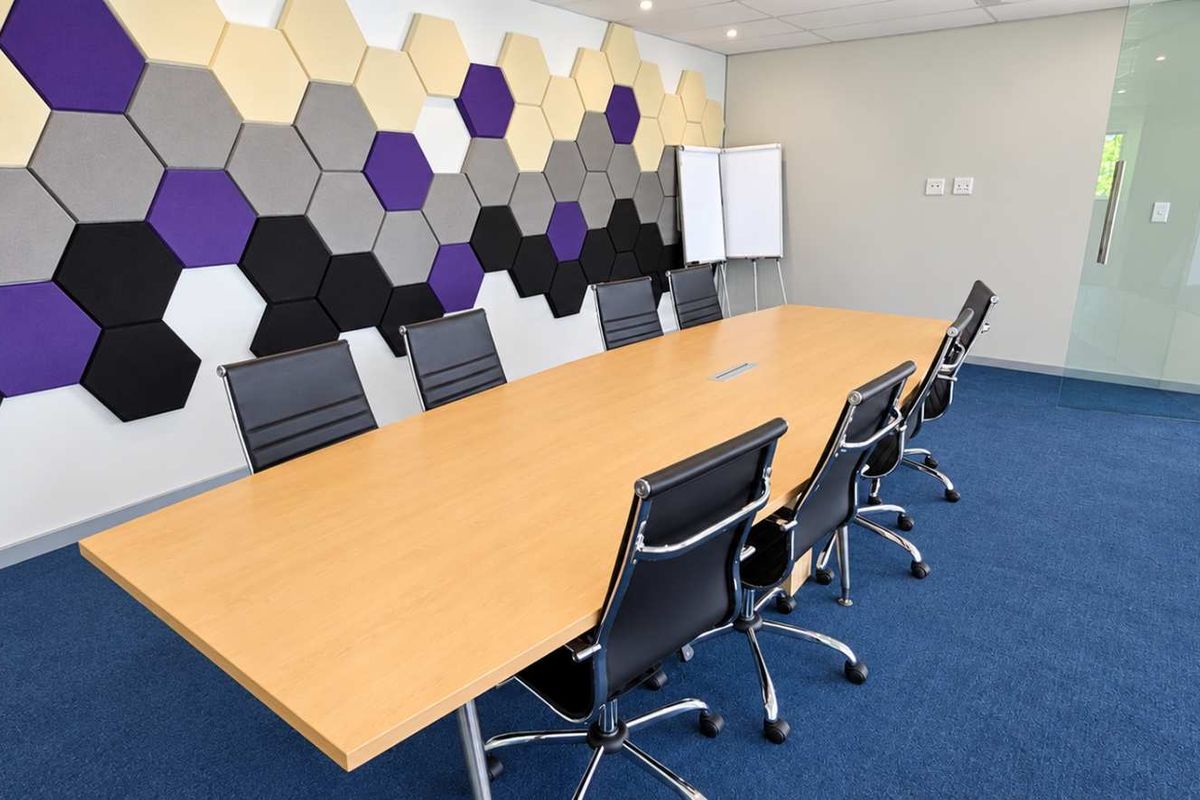 Modern office boardroom featuring acoustic hexagonal wall panels, blue carpeting, and a glass partition wall, providing a professional and functional meeting space.