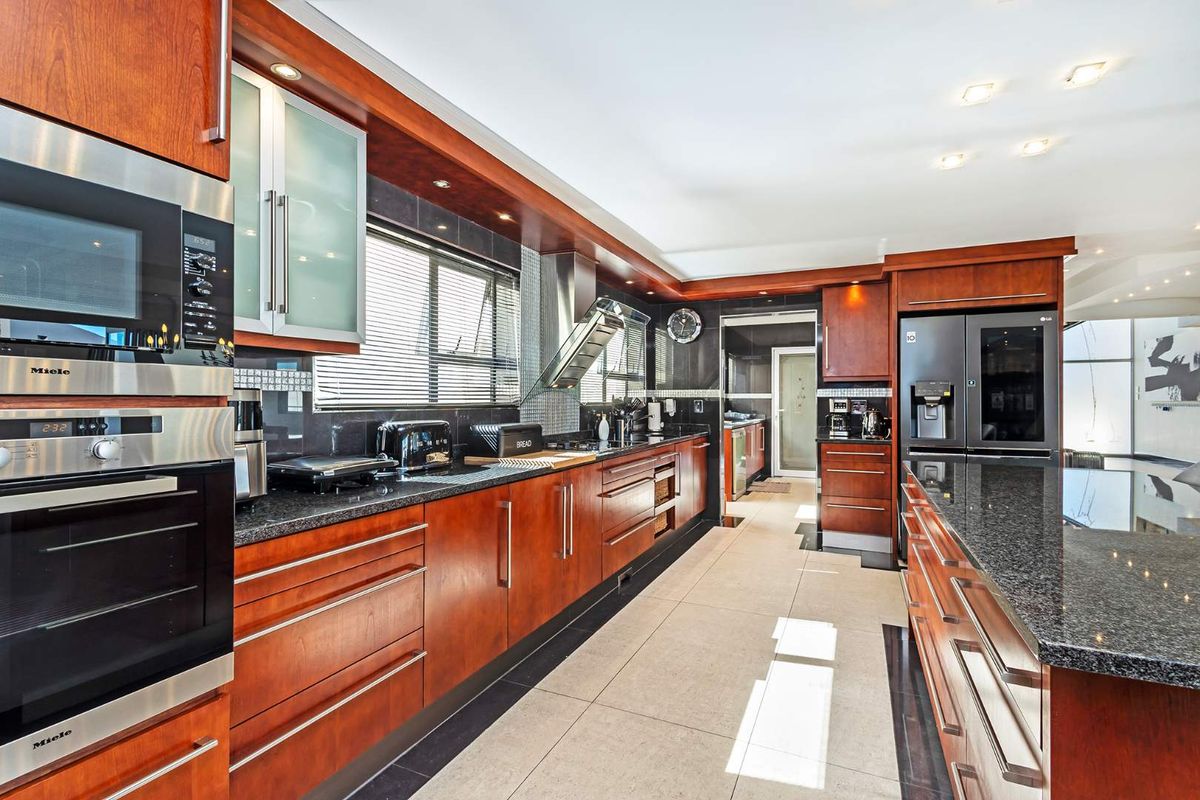 Spacious kitchen featuring rich wooden cabinetry, granite countertops, integrated Miele appliances, and modern recessed lighting with a clean, functional layout.