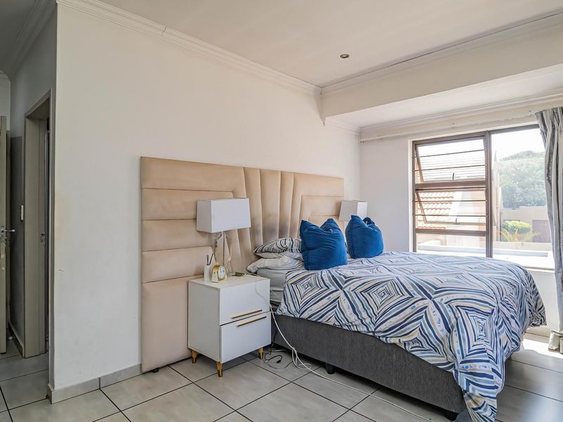 A well-lit bedroom featuring tiled flooring, recessed downlighting, and a large aluminium-framed window with views of the exterior.