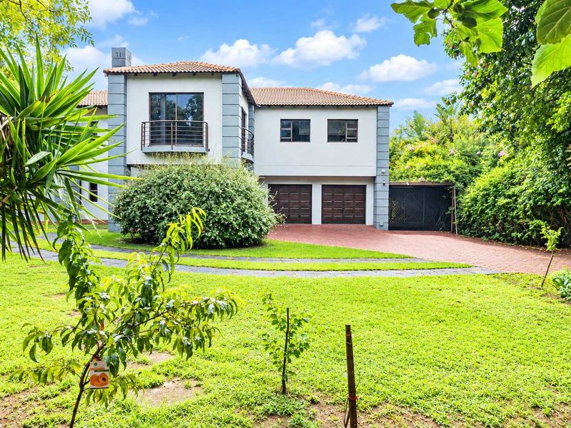 A well-maintained double-story residential property featuring a paved driveway, double garage, and a balcony, set within a lush, landscaped garden.