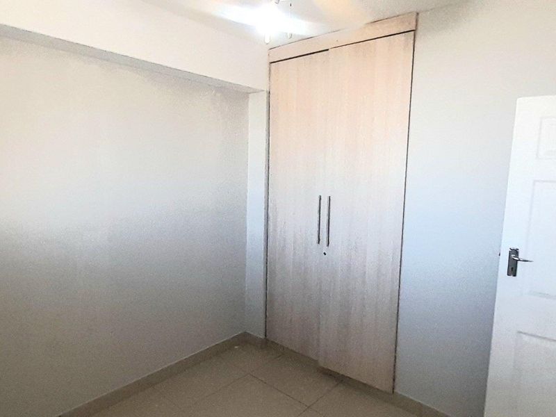 A clean, empty bedroom featuring neutral tiled flooring and built-in light wood-finish cupboards.