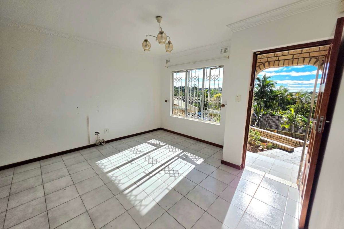 A bright, empty living area featuring tiled flooring, decorative ceiling cornices, and direct access to an outdoor patio space.