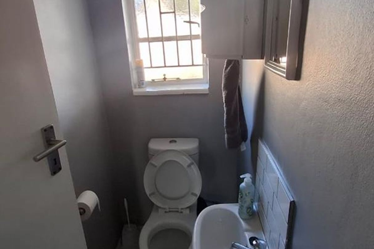 A compact office restroom featuring a wall-mounted basin, toilet, tiled flooring, and a window with security bars.