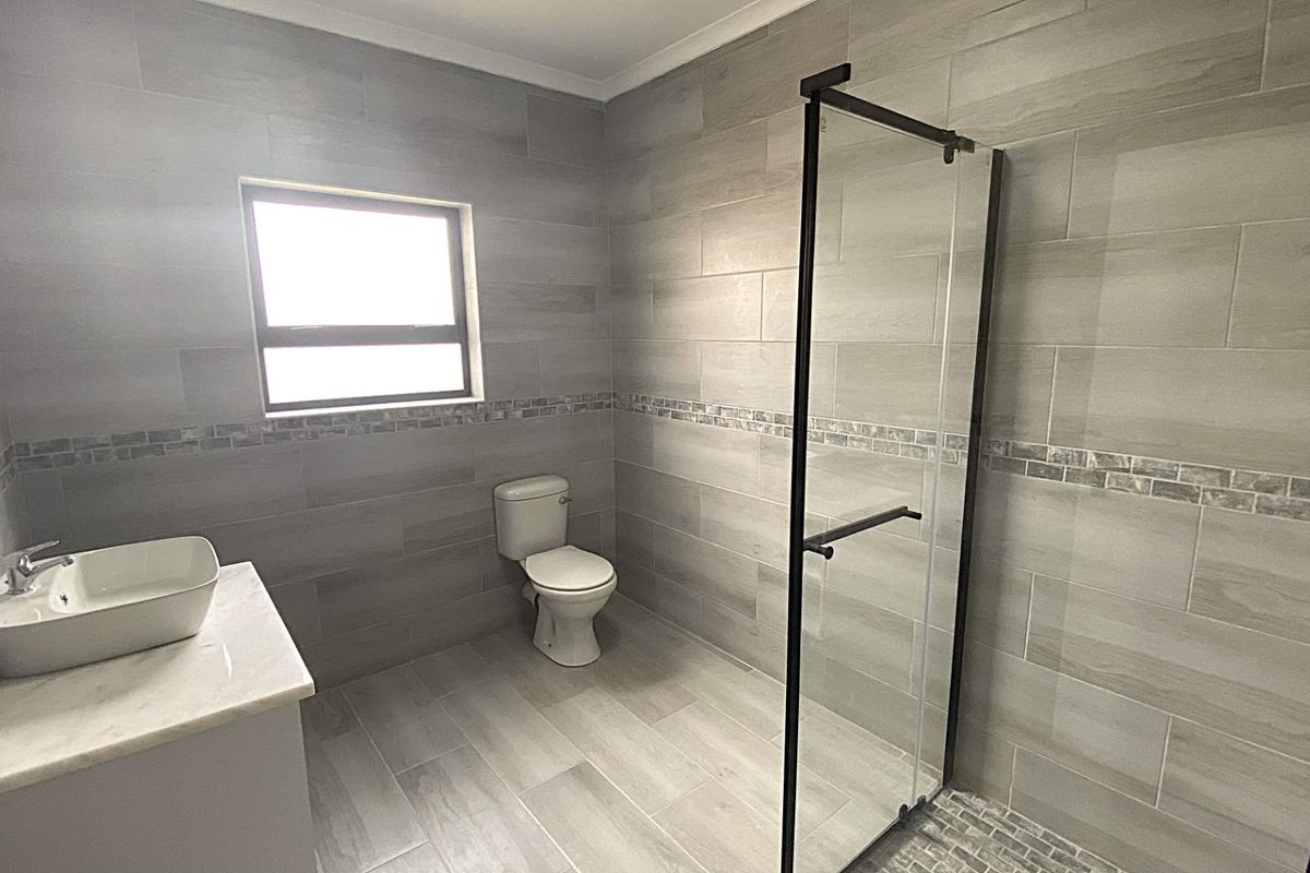 Modern bathroom featuring floor-to-ceiling grey wood-look tiling, a glass-enclosed walk-in shower, a contemporary vessel sink vanity, and a toilet.
