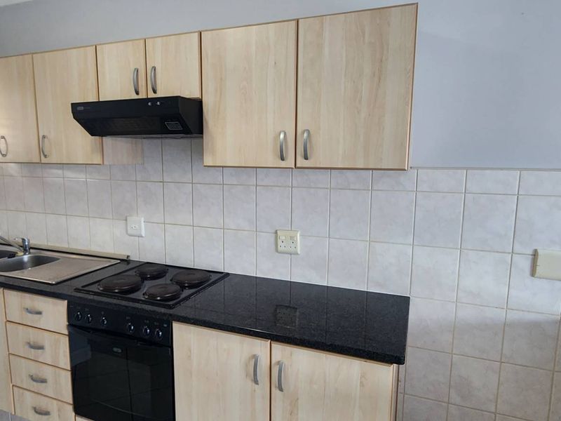 A functional kitchen featuring light wood-finish cabinetry, black granite countertops, a built-in oven and hob, and a tiled backsplash.