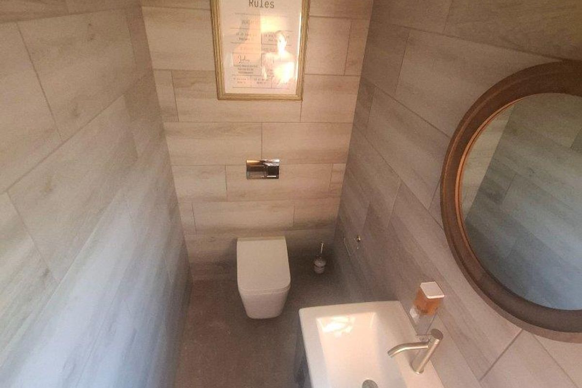 A modern powder room featuring wood-look wall tiles, a wall-mounted toilet with a concealed cistern, and a sleek vanity basin.