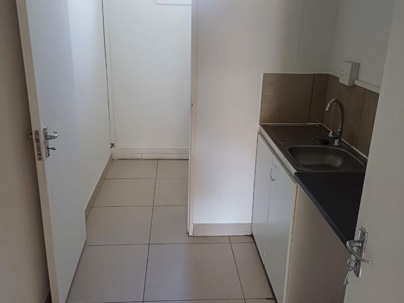 A compact kitchenette area featuring a small sink, base cabinetry, and tiled flooring, leading into an adjacent utility space.