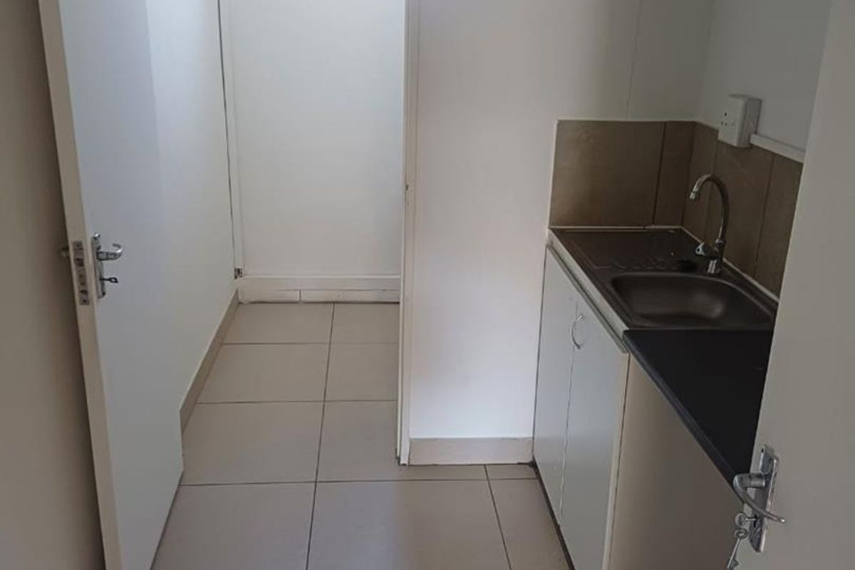 A compact kitchenette area featuring a small sink, base cabinetry, and tiled flooring, leading into an adjacent utility space.
