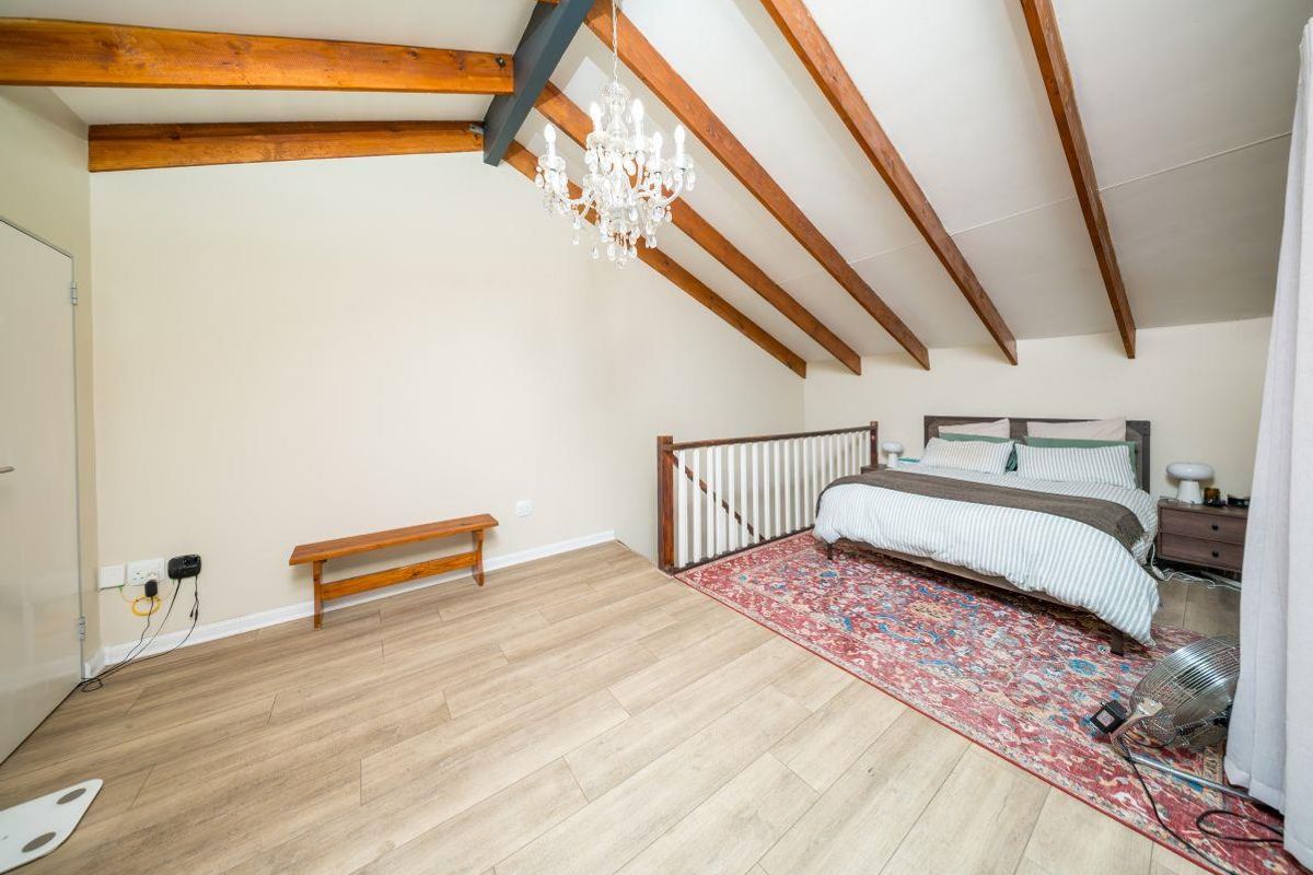 Spacious loft-style bedroom featuring vaulted ceilings with exposed timber rafters, timber laminate flooring, and a protective timber balustrade overlooking the lower level.