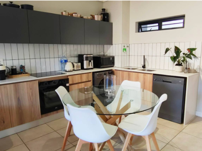 Modern open-plan kitchen featuring sleek dark upper cabinetry, wood-finish lower cabinets, integrated appliances, and a tiled backsplash, seamlessly connected to the dining area.