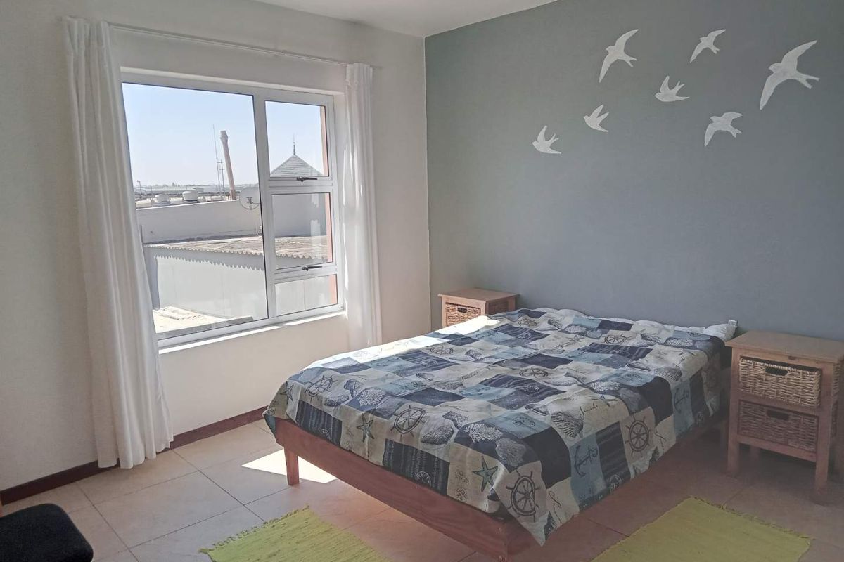 A bright bedroom featuring tiled flooring, a large window with natural light, and a neutral grey accent wall.